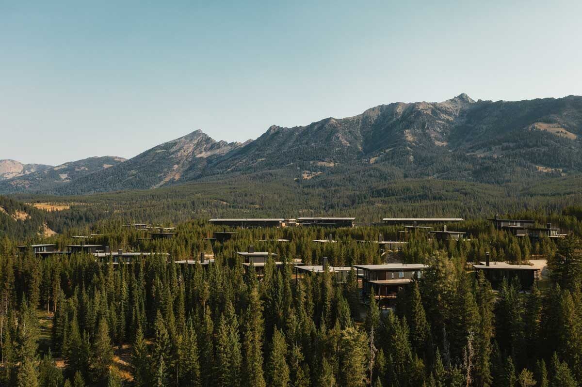Un moderno complejo turístico con varias construcciones en medio de un paisaje boscoso y montañas al fondo.