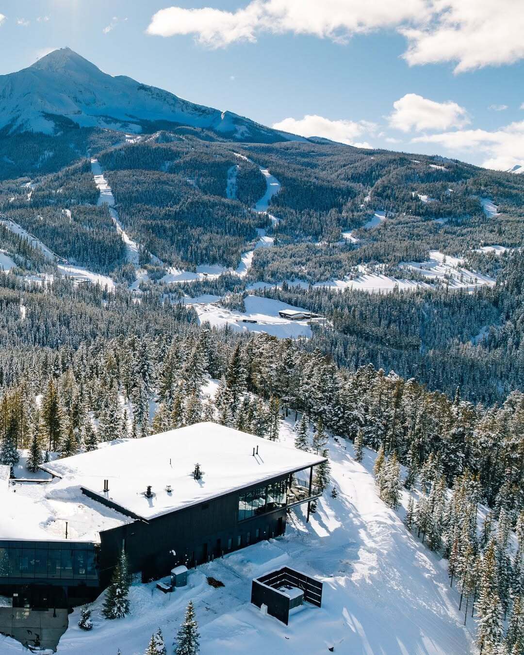 Ein modernes Gebäude mit flachem Dach, umgeben von schneebedeckten Bäumen und einem Berg im Hintergrund.