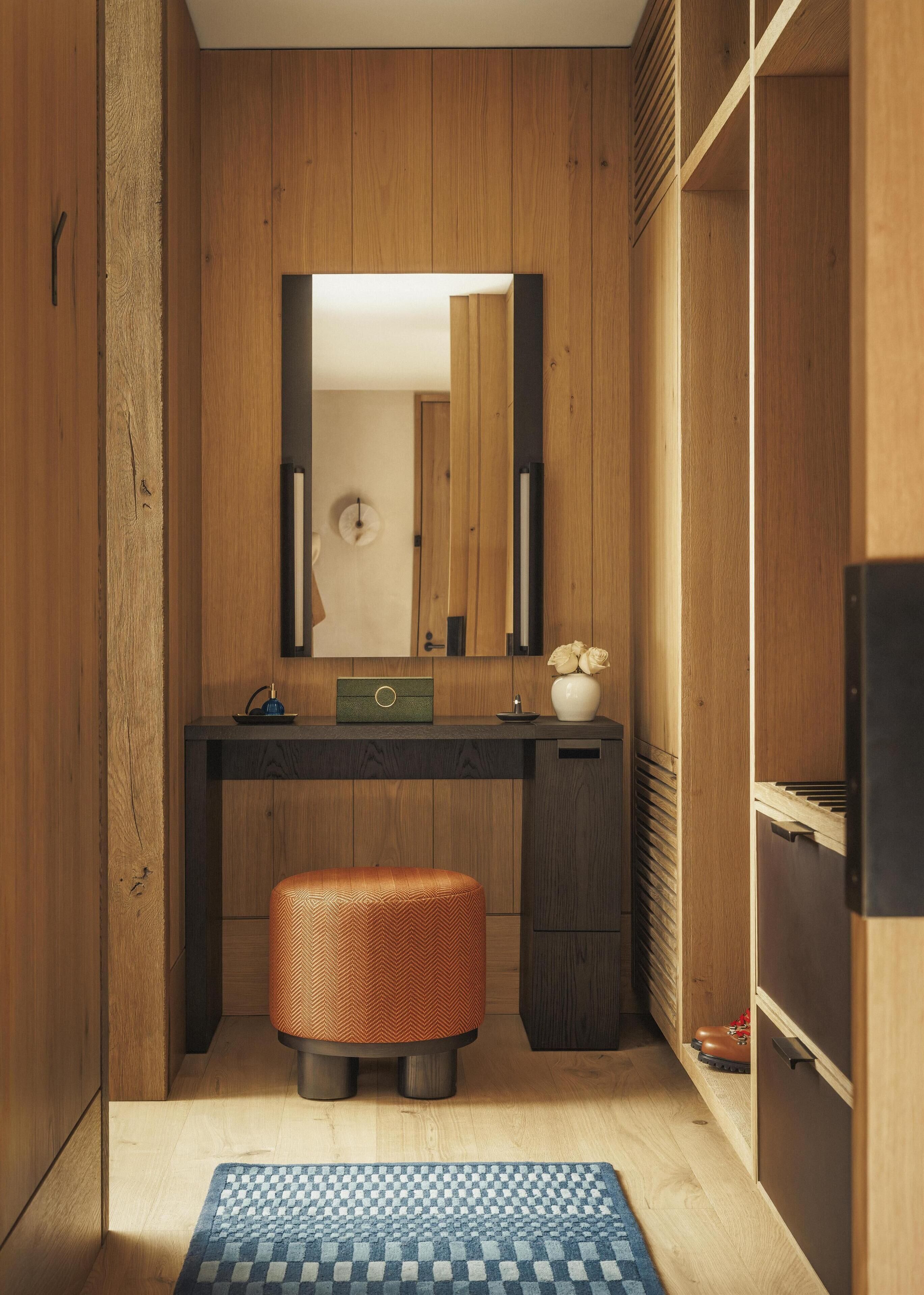 Un baño pequeño con paredes de madera, un espejo, un lavabo, un taburete y una alfombra a cuadros.