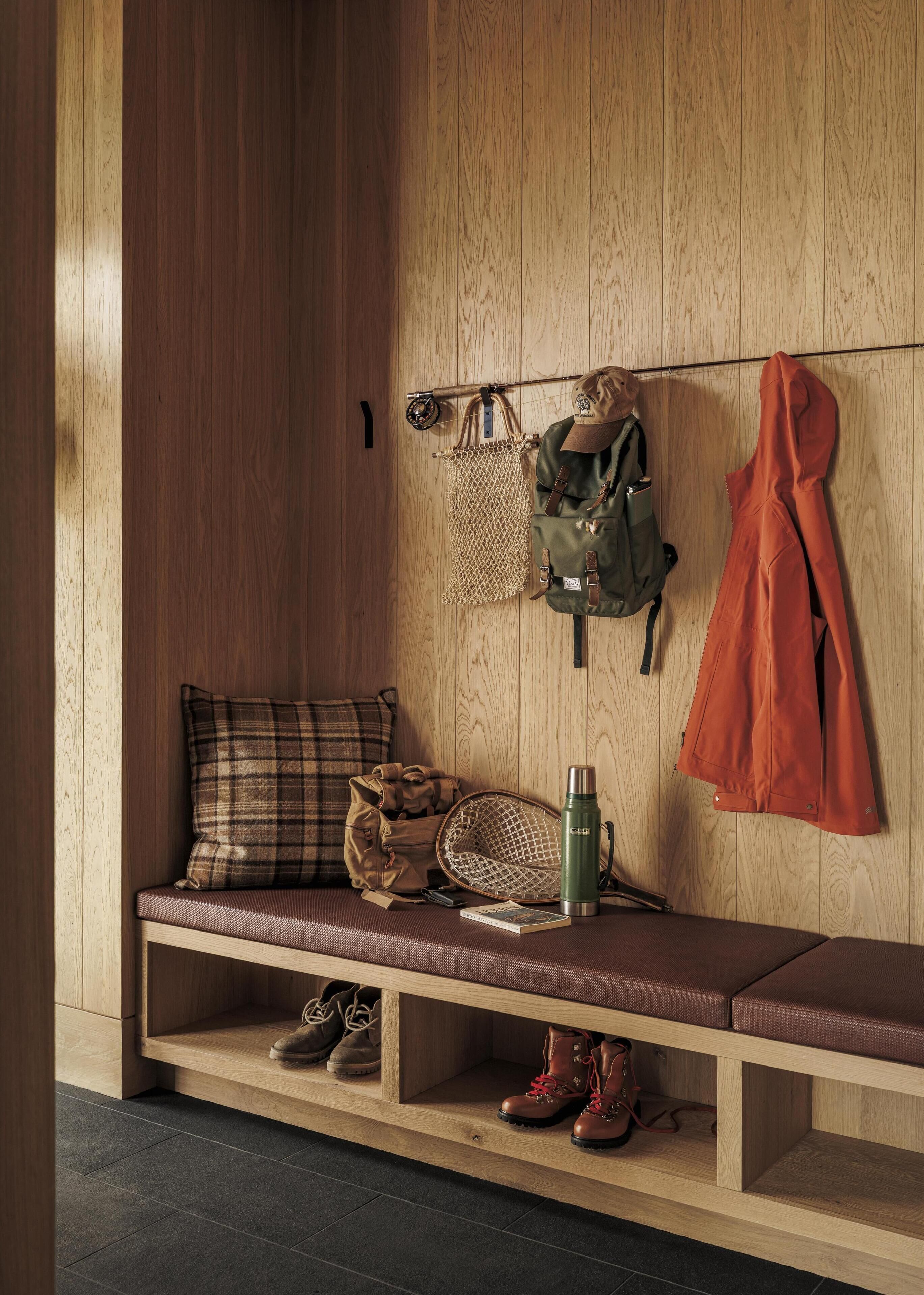 Een houten bank met een geruit kussen, een groene thermosfles en een paar laarzen.