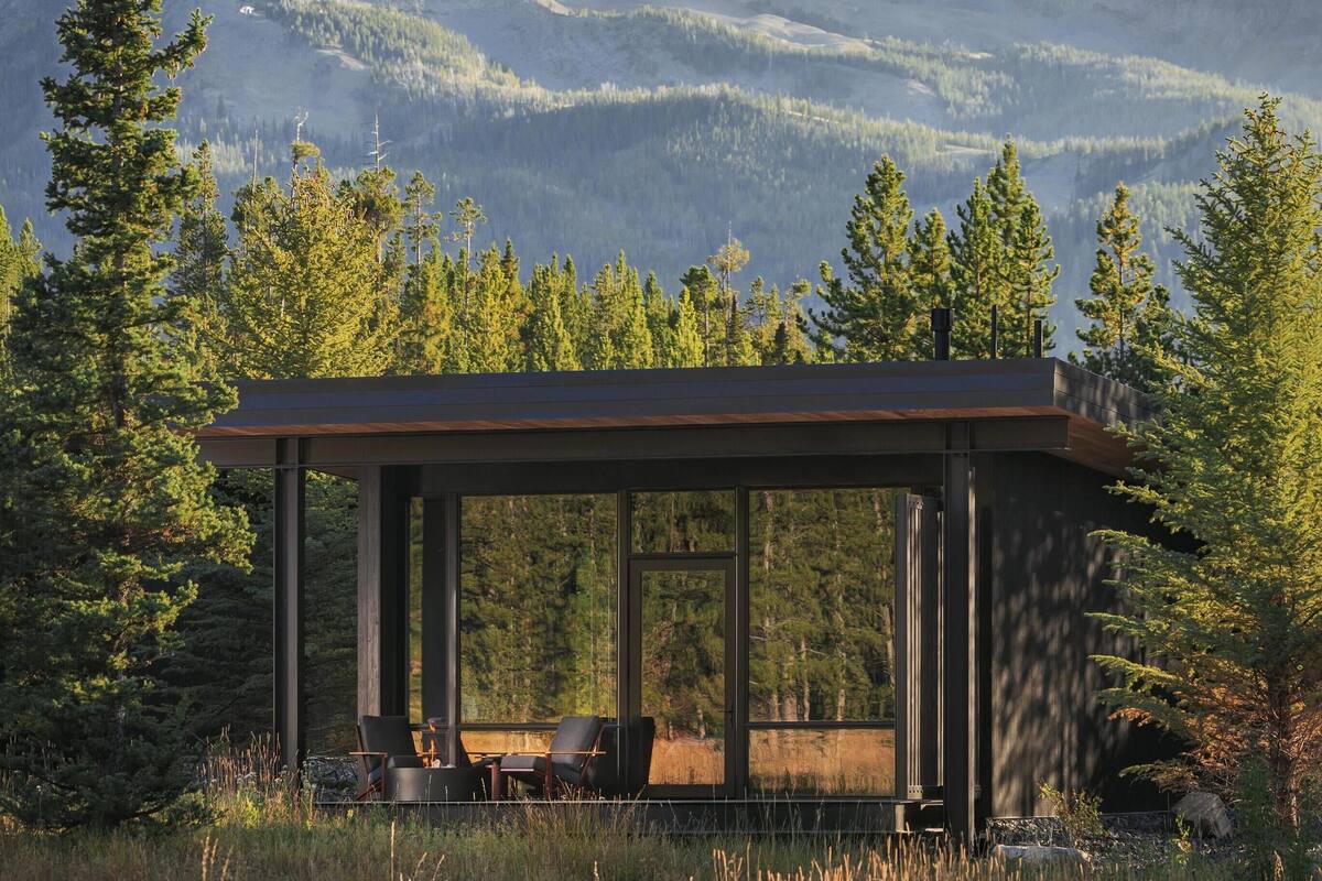 A modern cabin with a glass enclosure, situated in a forested area with a mountain in the background.