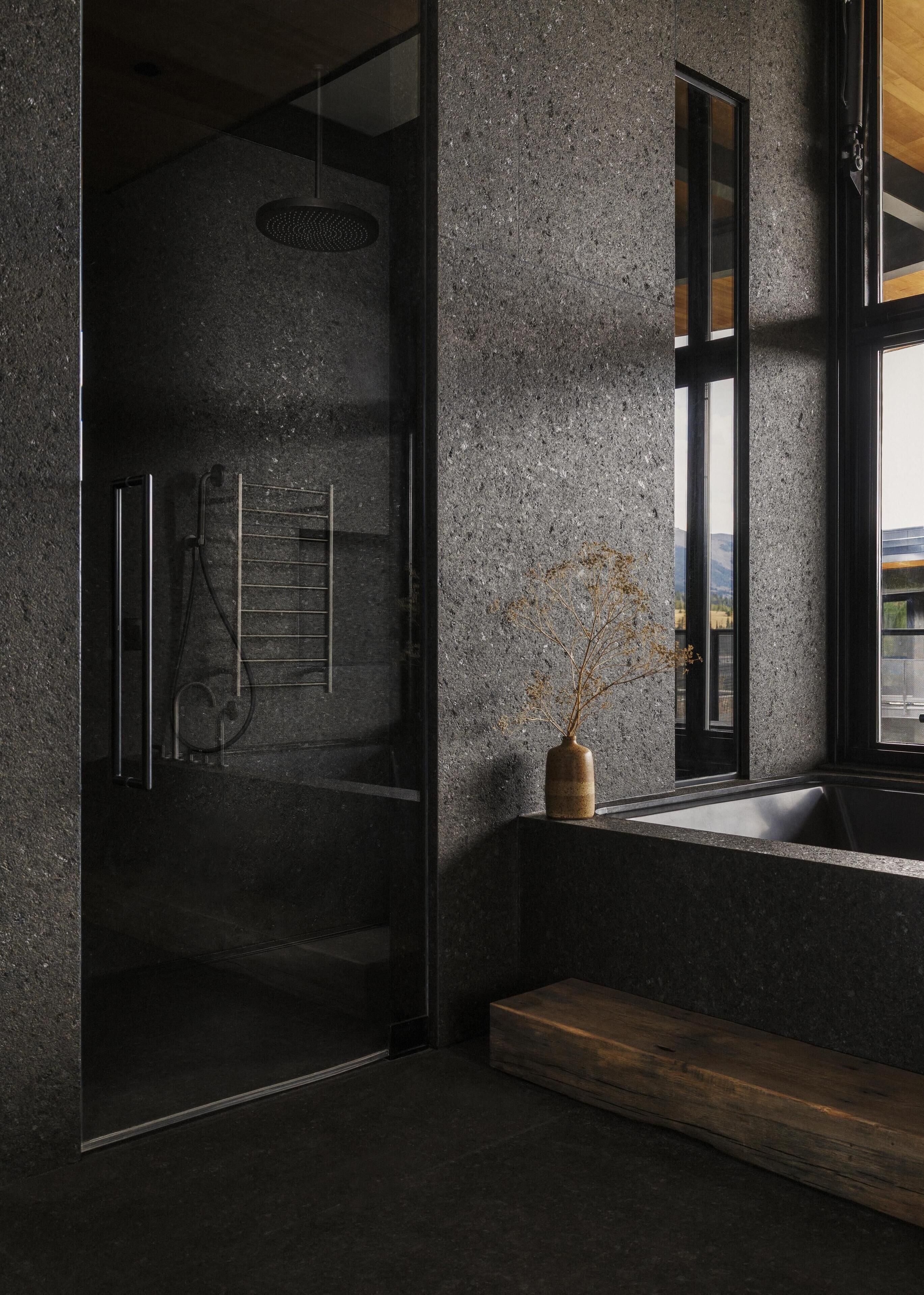 Une salle de bain moderne avec une douche à l’italienne en verre, un banc en bois et un vase contenant des branches séchées, posé sur une étagère.