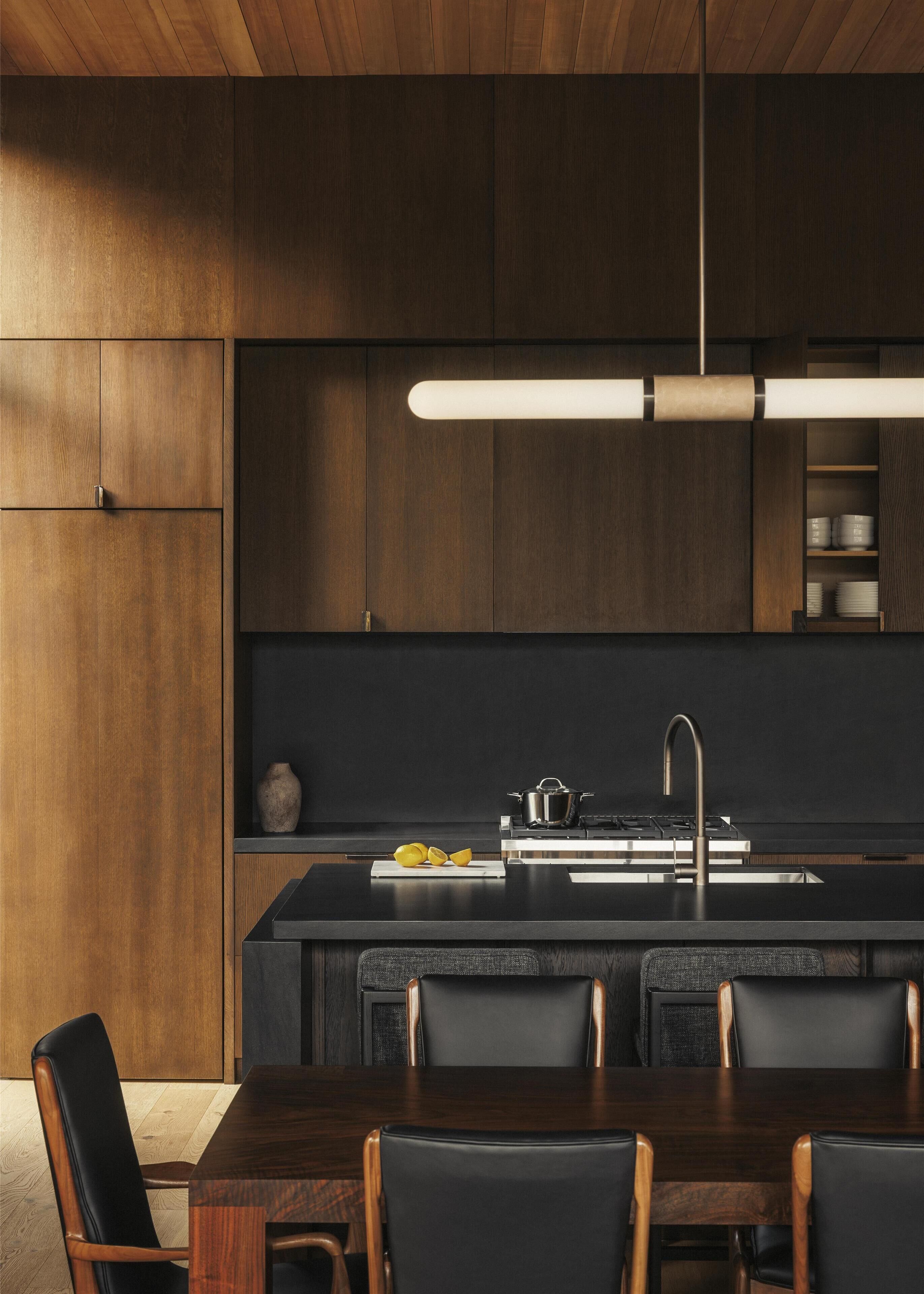 Una cocina moderna con armarios de madera oscura, una isla central con pileta y un comedor con mesa y sillas de madera.