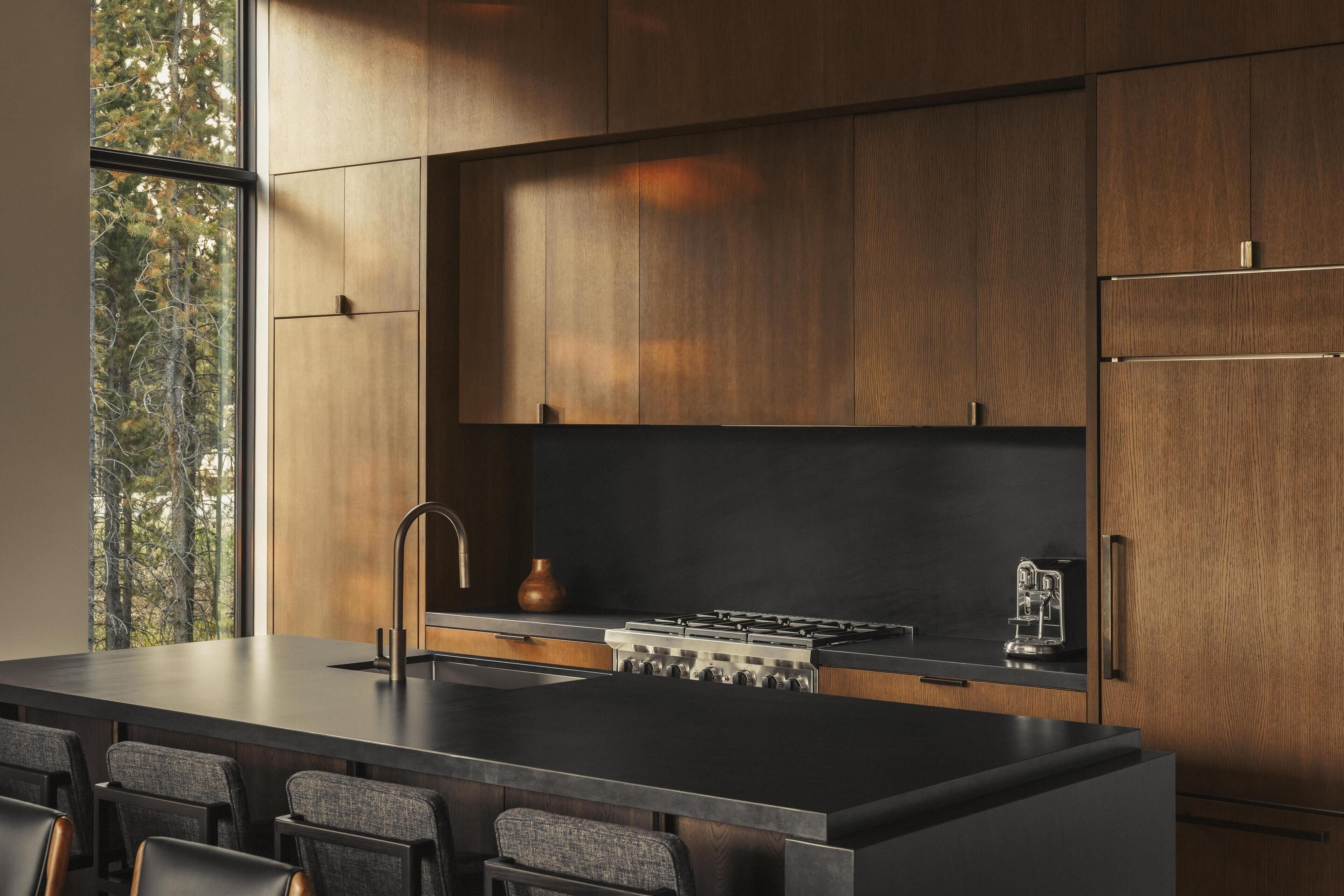 A modern kitchen with a large island, dark countertops, and wooden cabinets.