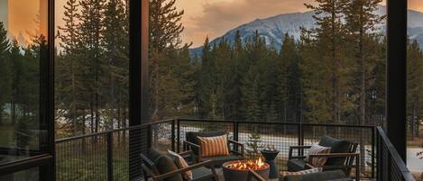 A deck with outdoor furniture and a fire pit, overlooking a forest and mountains.