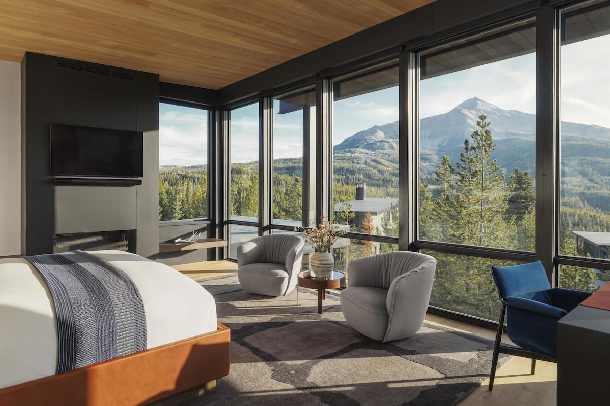 A modern bedroom with a large window, a bed, a TV, and a view of a mountain.