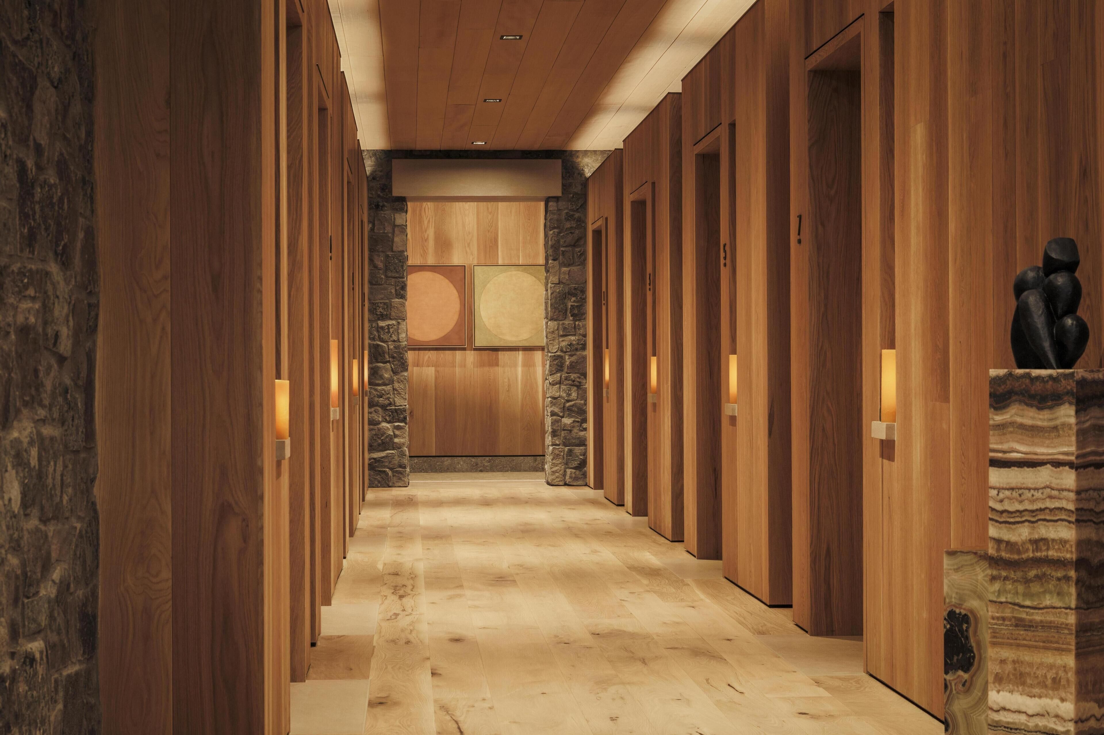 A hallway with wooden paneling and stone accents, leading to a room with a large window and a stone wall.