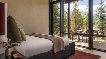 Un dormitorio moderno con una cama grande, vistas a una terraza con mobiliario exterior y montañas al fondo.