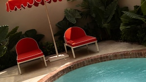 Une piscine dans laquelle une personne nage, entourée de chaises rouges et d’un parasol orange.
