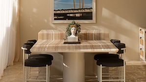 Un coin repas avec une table, des chaises et un tableau encadré représentant des palmiers.