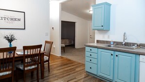Una cocina con armarios azul claro, una mesa de comedor de madera con sillas y un cartel enmarcado en la pared.