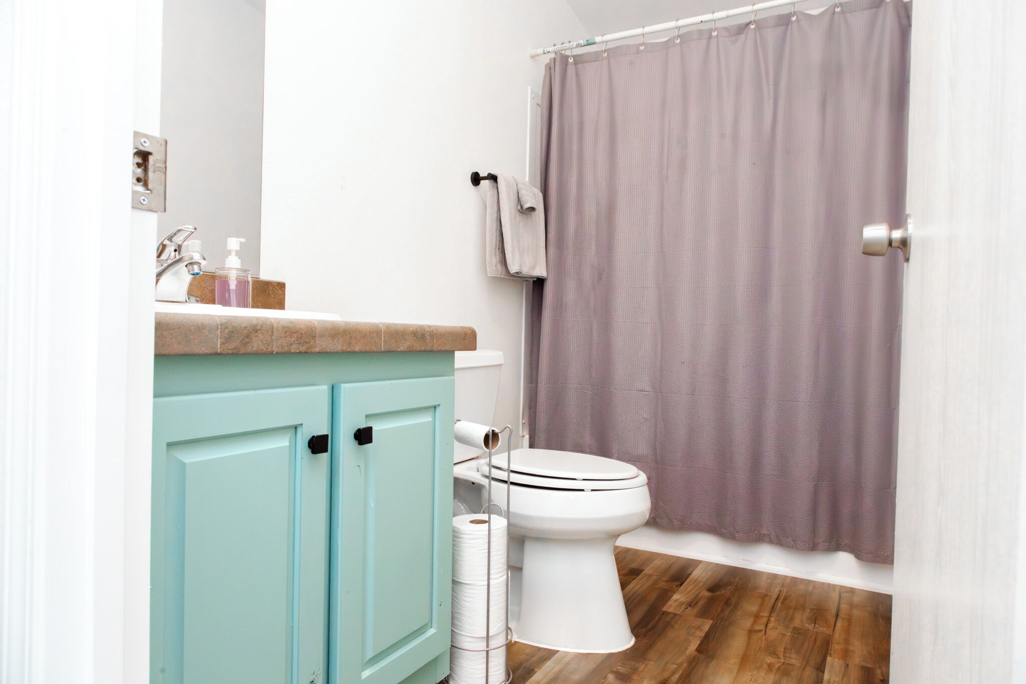 Een badkamer met toilet, een wastafel met zeepdispensers, een handdoekrek en een douchegordijn.