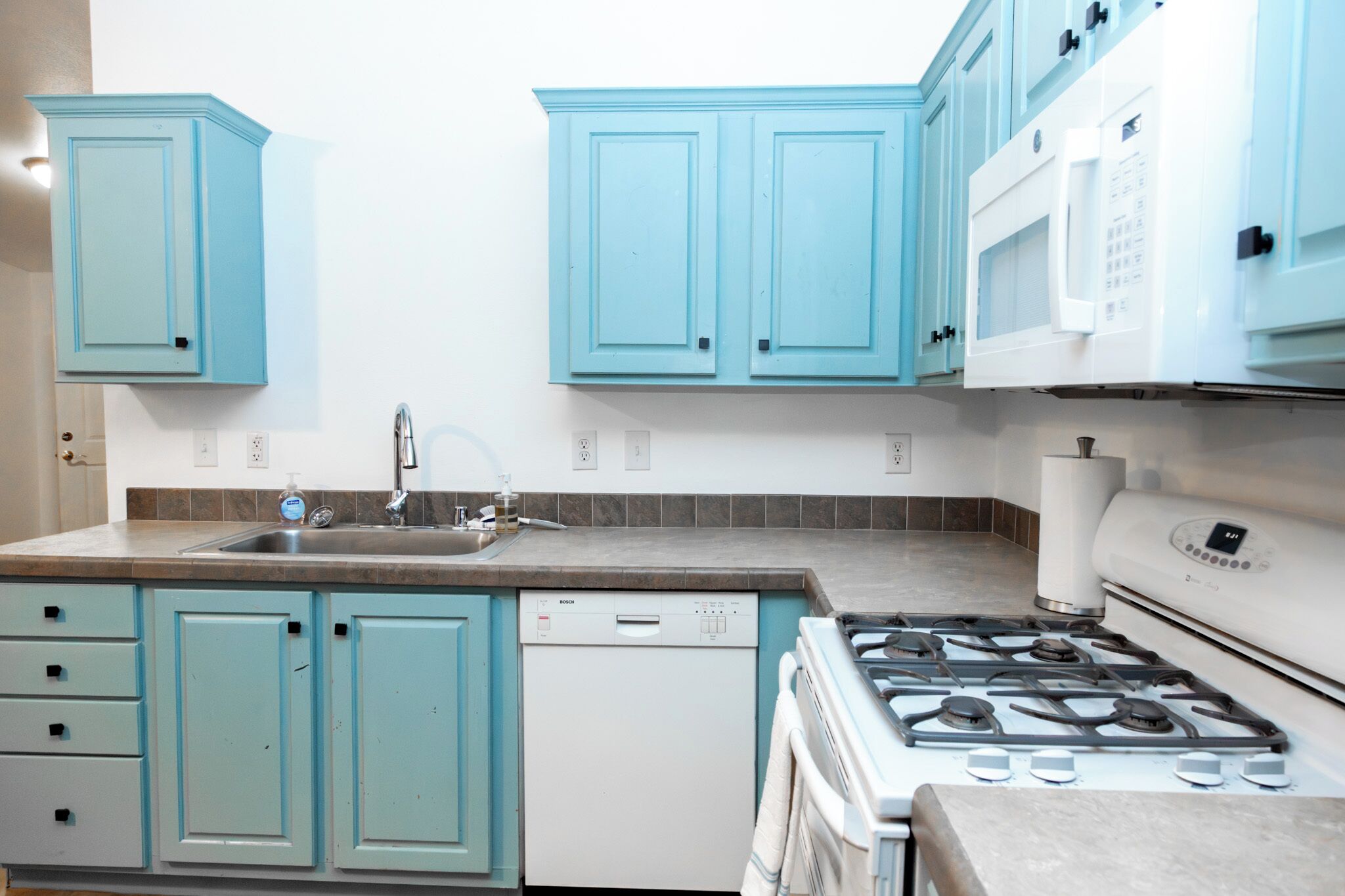 A kitchen with teal cabinets, a white dishwasher, a stove, and a microwave.
