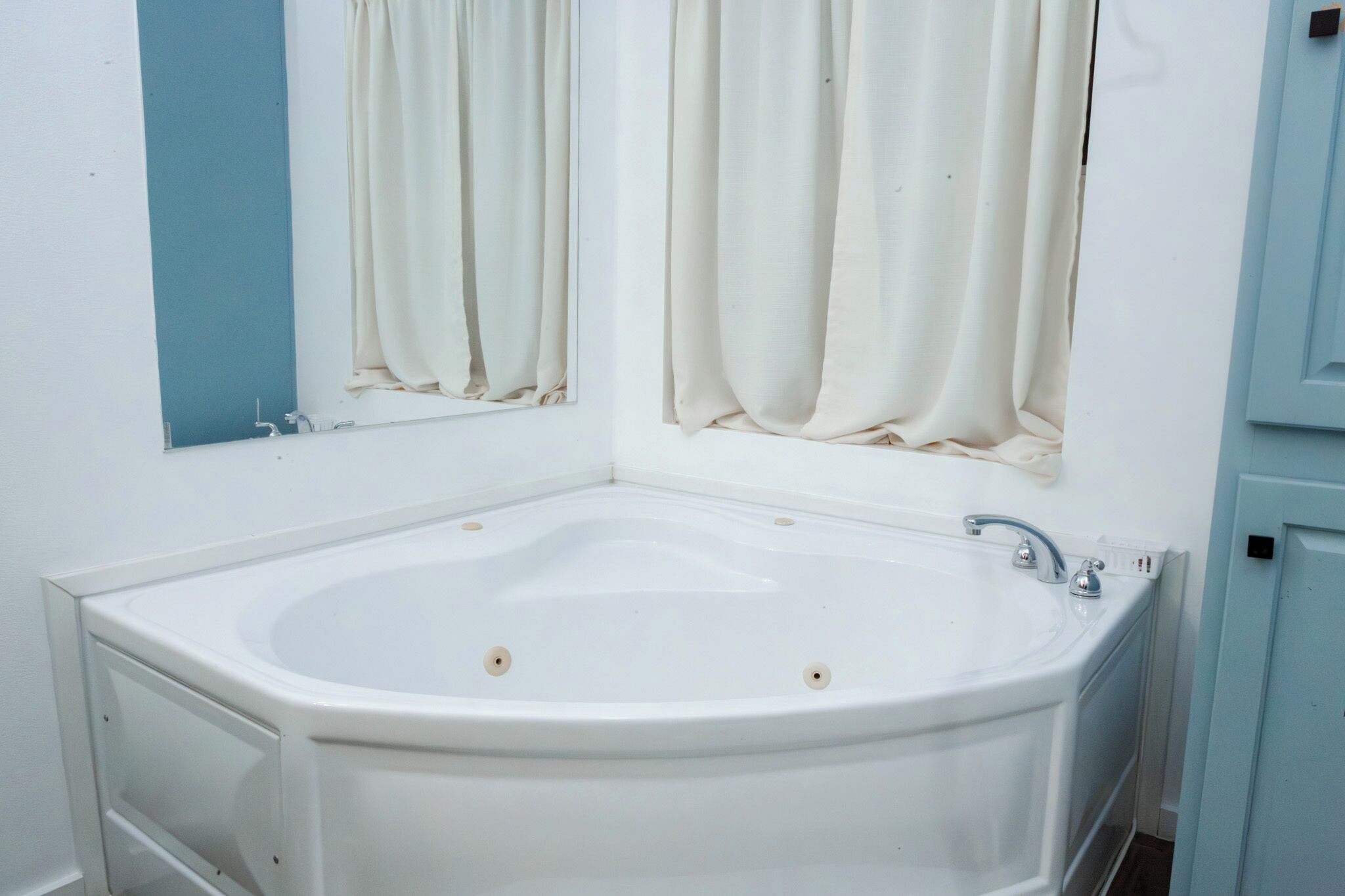 A bathroom with a freestanding bathtub, a mirror, and a window with curtains.