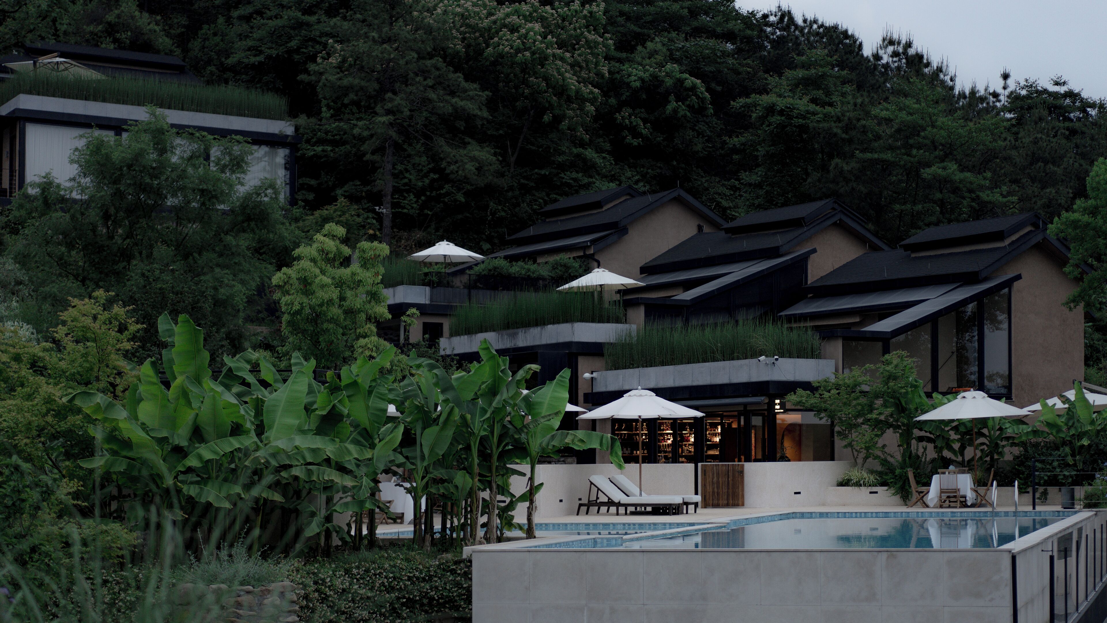A modern hotel with a pool, surrounded by lush greenery and a restaurant.