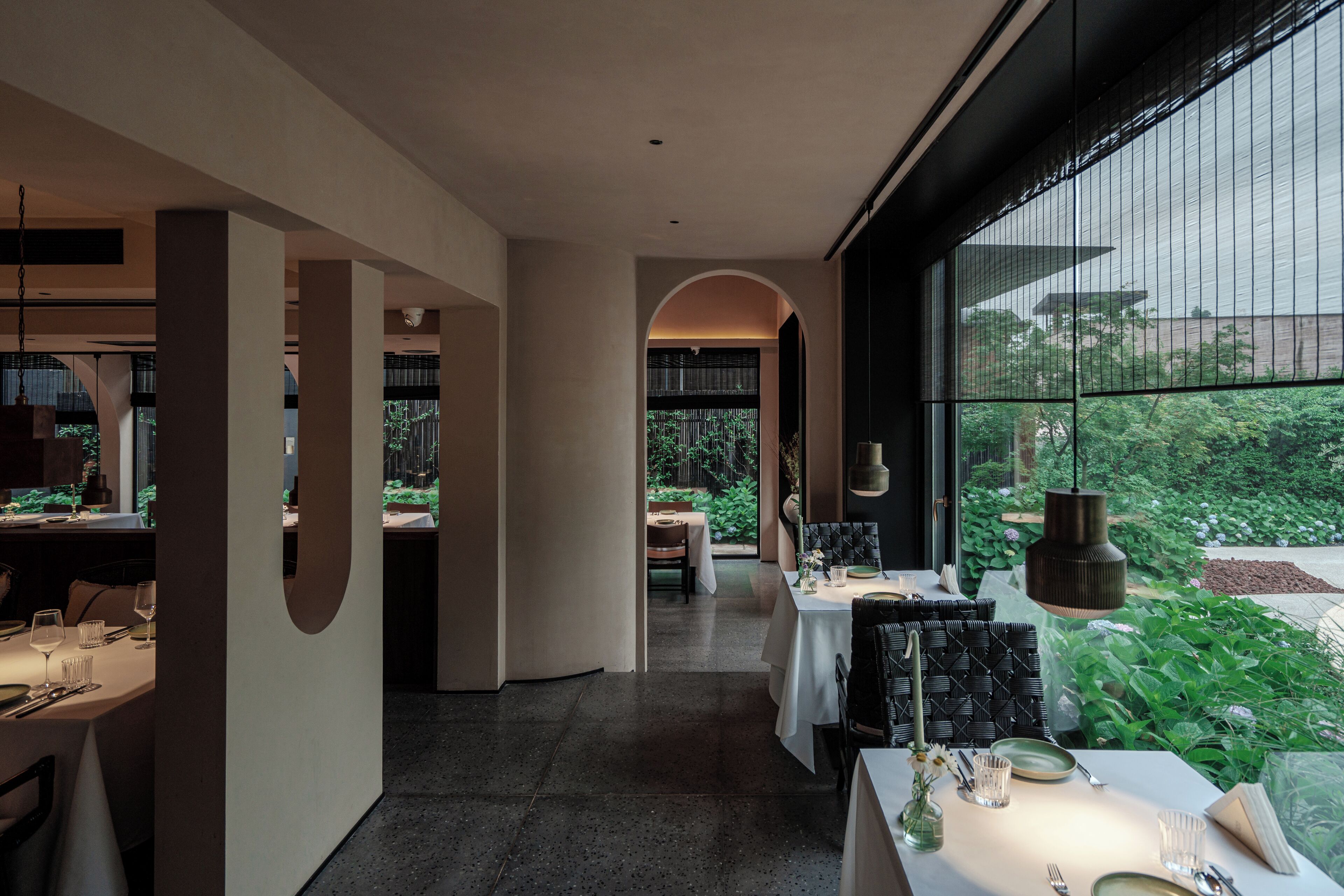 Zona pranzo moderna con un tavolo lungo, sedie e vista su piante verdi all'esterno.