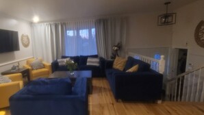 A living room with a blue sofa set, a yellow armchair, and a flat-screen TV mounted on the wall.