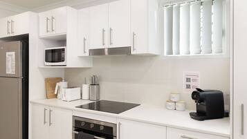 A modern kitchen with white cabinets, a stainless steel refrigerator, a microwave, a toaster, a coffee machine, and a built-in oven.