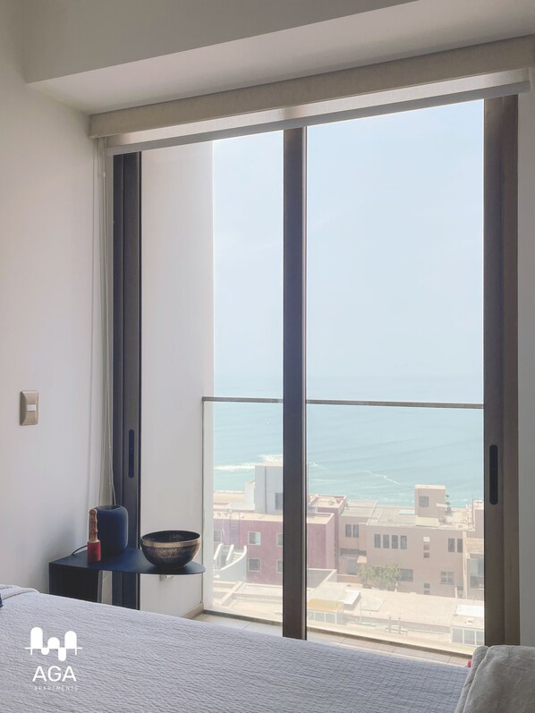 A bedroom with a large window overlooking a cityscape and the sea.