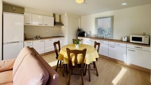 Una cocina compacta con armarios blancos, una mesa de comedor con sillas, un microondas y un tostador.