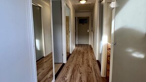 Un pasillo con suelo de madera, paredes blancas y puertas que dan a habitaciones.
