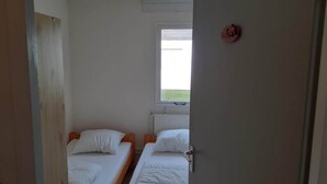 Una habitación con dos camas individuales, una ventana con vistas a zonas verdes y una puerta con pomo redondo.