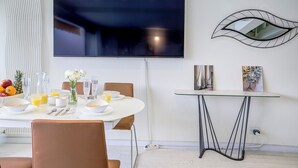 A dining area with a round table, chairs, and a TV mounted on the wall. There are two paintings on the wall and a power outlet visible. - Le Lido, Spectacular Beachfront Cap Ferrat  (Saint-Jean-Cap-Ferrat)
