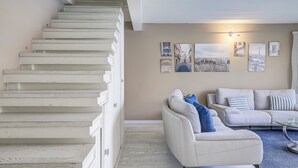 A staircase leading to an upper floor, a living room with a sofa and a coffee table, and a wall with framed cityscape pictures. - Le Lido, Spectacular Beachfront Cap Ferrat  (Saint-Jean-Cap-Ferrat)