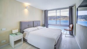 A bedroom with a large bed, a nightstand, a chair, and a view of the sea. - Le Lido, Spectacular Beachfront Cap Ferrat  (Saint-Jean-Cap-Ferrat)