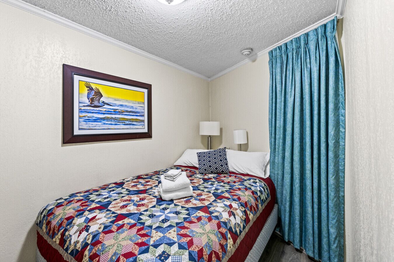 Une chambre d’hôtel avec un lit, deux lampes de chevet, un tableau encadré et un rideau bleu.