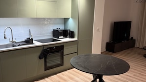 A modern kitchen with a built-in oven, a coffee maker, and a microwave. There is a round table with a black marble top in the center of the room. - Cozy 1 bed apartmrnt  Luton Airport (Luton)