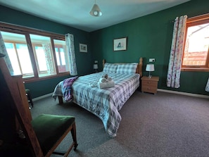 Ein Schlafzimmer mit einem Bett, Nachttischen, einem Sessel und einem Fenster mit Vorhängen.