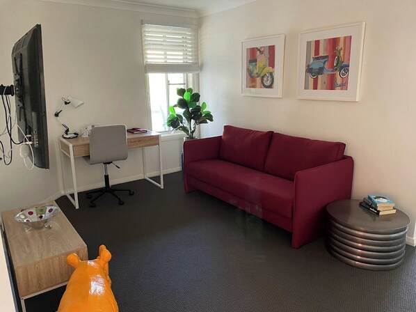 A modern living room with a red sofa, a desk with a computer, a plant, and artwork on the wall.