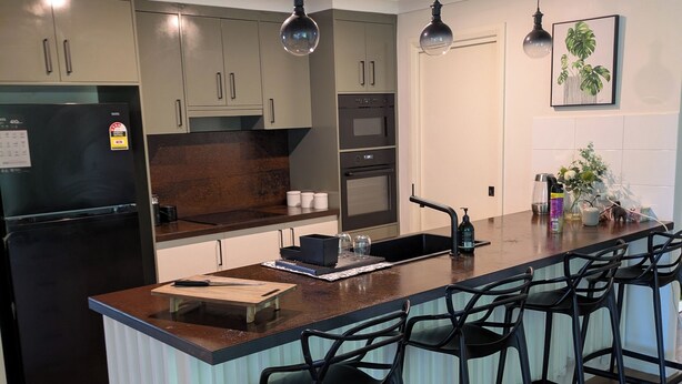 Uma cozinha moderna com uma ilha central, banquetas, frigorífico, forno e luzes pendentes.