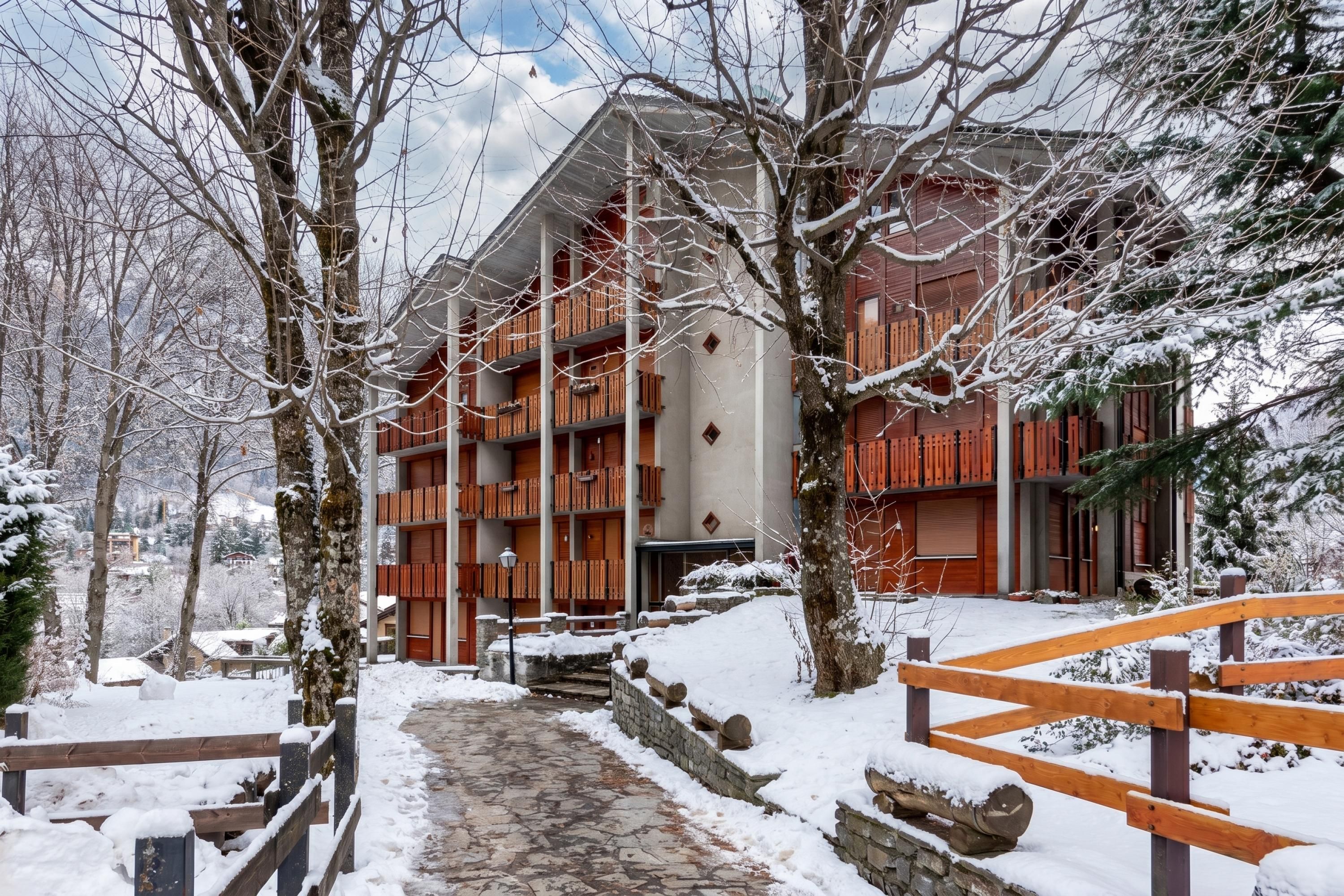 A multi-story building with a stone pathway leading to the entrance, surrounded by snow-covered trees.