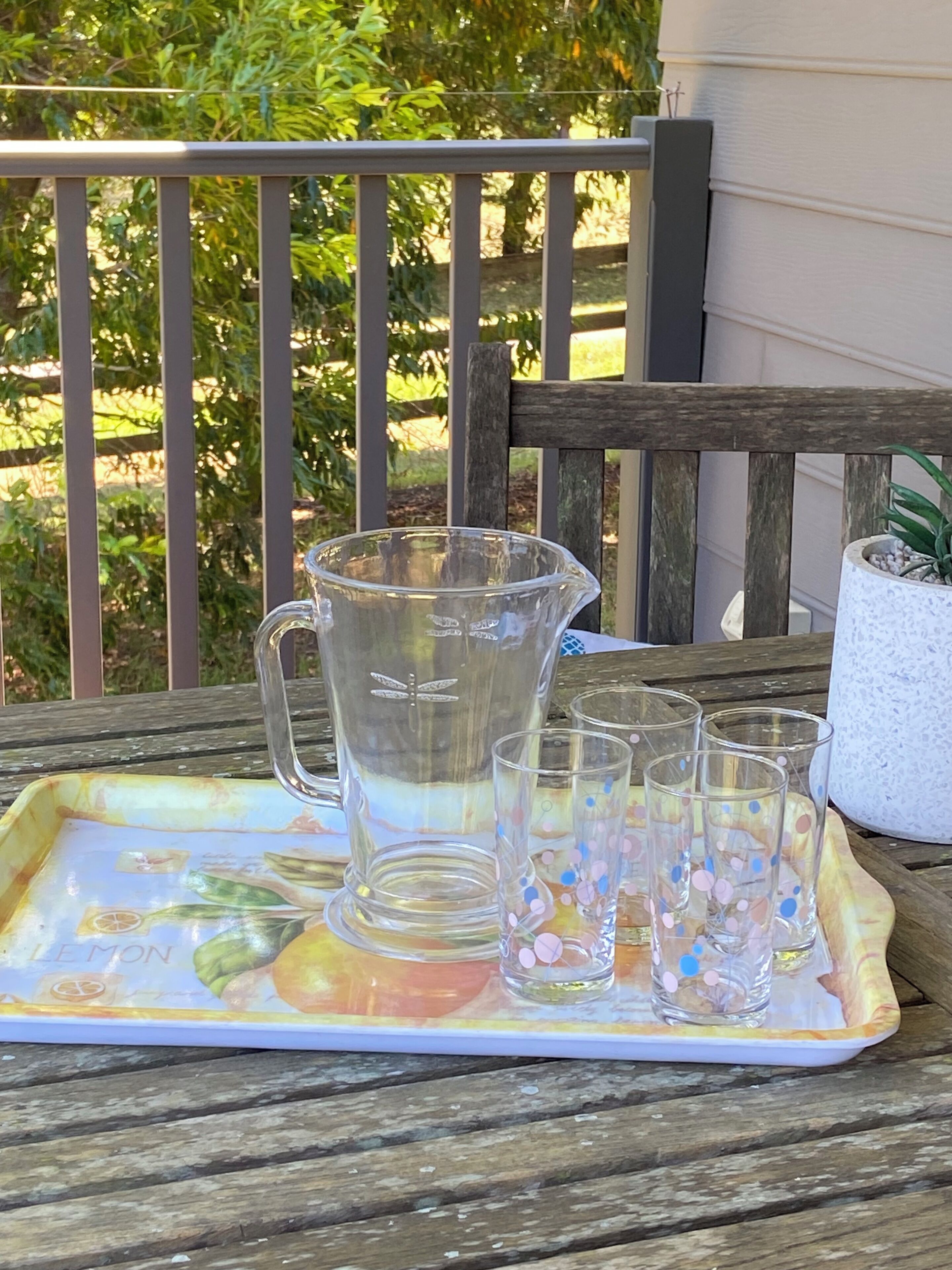 A tray with a pitcher and glasses on a wooden table outdoors.