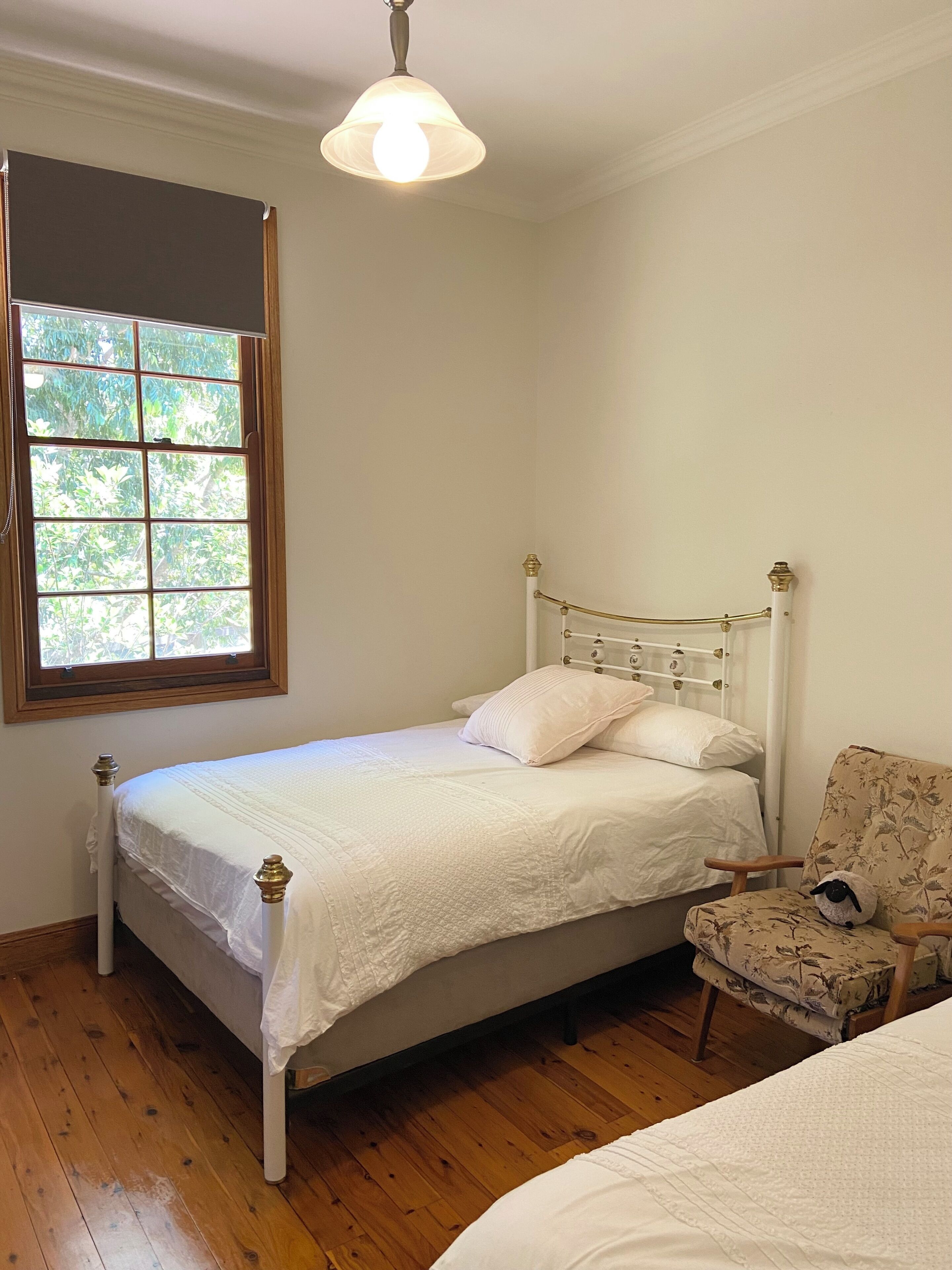 Une chambre avec un lit simple, une chaise, une fenêtre donnant sur un espace verdoyant et un luminaire au plafond.