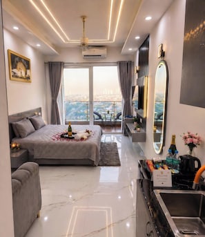 A modern hotel room with a bed, a sitting area, a balcony with a view, a minibar, and a large mirror. - The Cosette Corner @Gaur city center (Greater Noida)