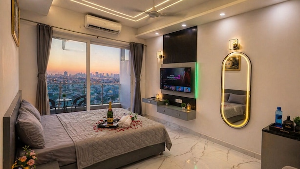 A modern hotel room with a large bed, a TV, a mirror, and a city view. - The Cosette Corner @Gaur city center (Greater Noida)