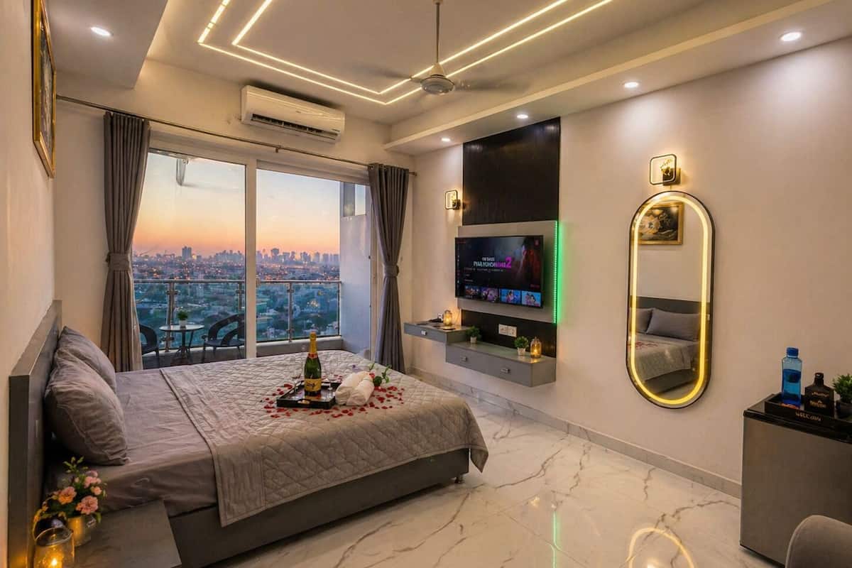 Una habitación de hotel moderna con una cama grande, televisión, espejo y vista a la ciudad.
