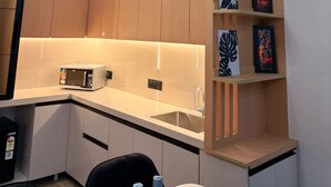 A modern kitchen with wooden cabinets, a built-in microwave, a sink, and a pendant light. - The Cosette Corner @Gaur city center (Greater Noida)