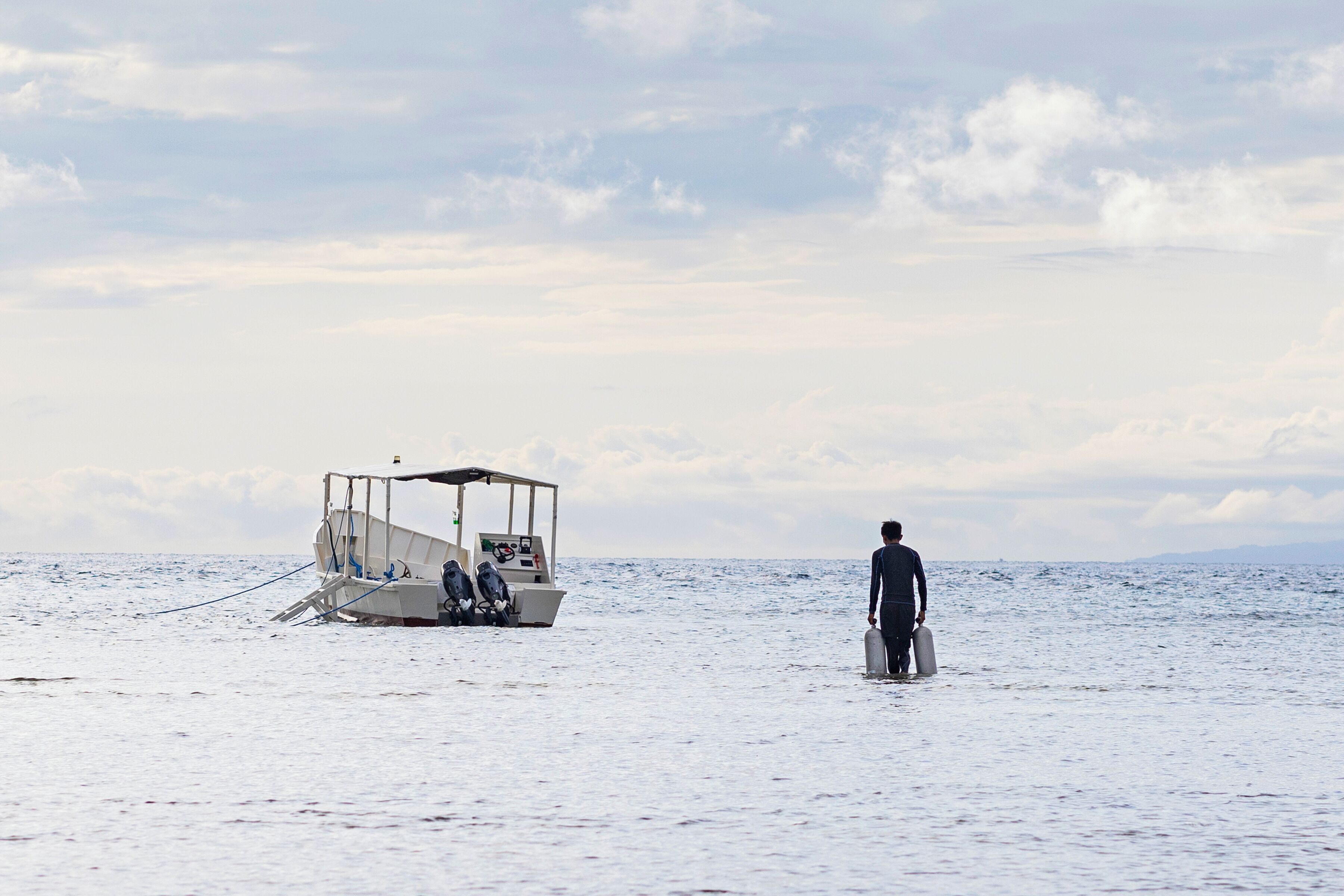 A boat anchored in calm waters with a person carrying a suitcase walking towards it.