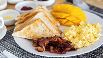 Une assiette avec des toasts, des œufs brouillés, du bacon et une mangue.
