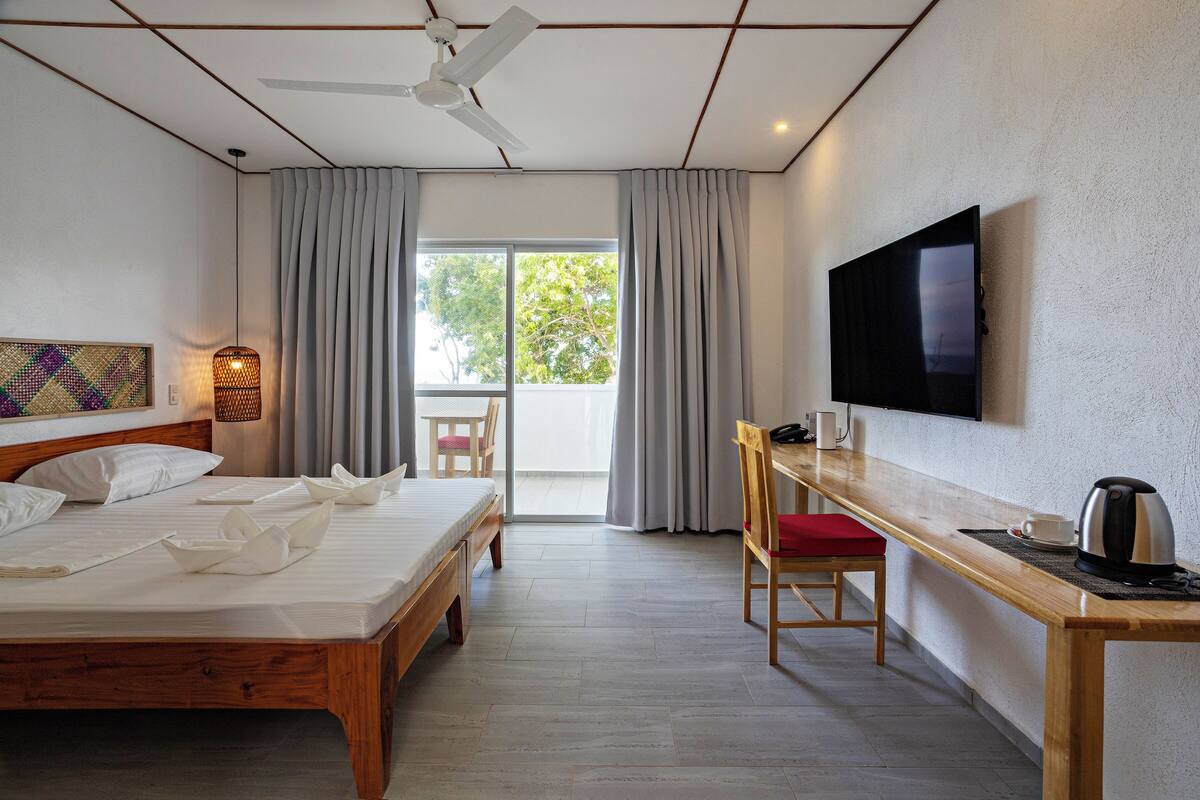 A hotel room with a bed, a desk, a chair, a TV, and a view of the outdoors.