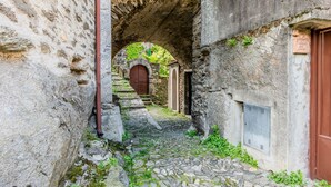 A narrow stone pathway under an arched structure, leading to a wooden door. - Castello by Interhome (Dervio)