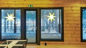 Puinen mökki, jonka sisätiloissa on suuret ikkunat, tähtimäiset valaisimet ja pöytä tuoleineen.