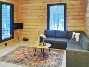 A log cabin interior with a sofa, a small table, a TV, and a large window.