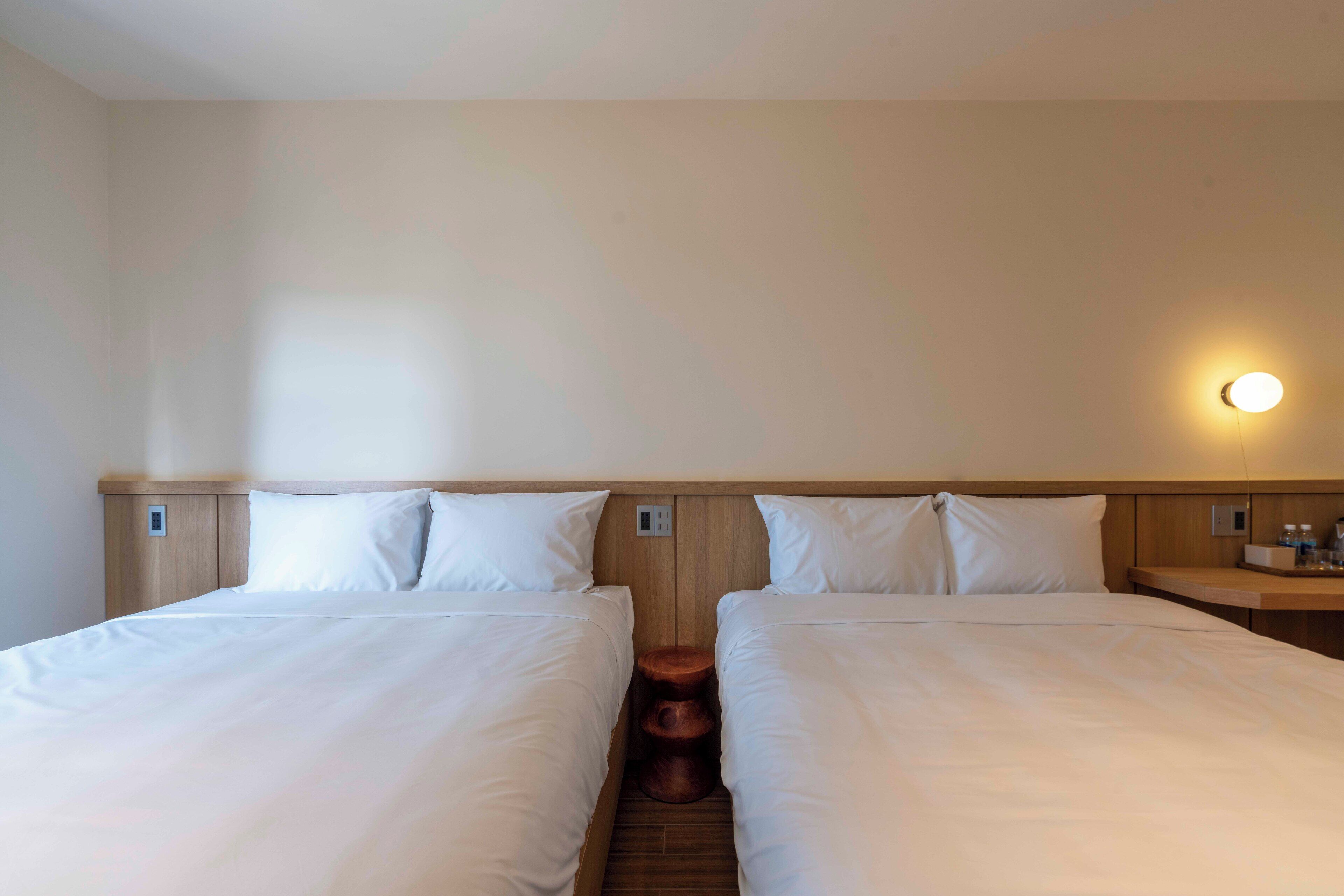 Een hotelkamer met twee bedden, een houten hoofdbord, een nachtkastje en een wandlamp.