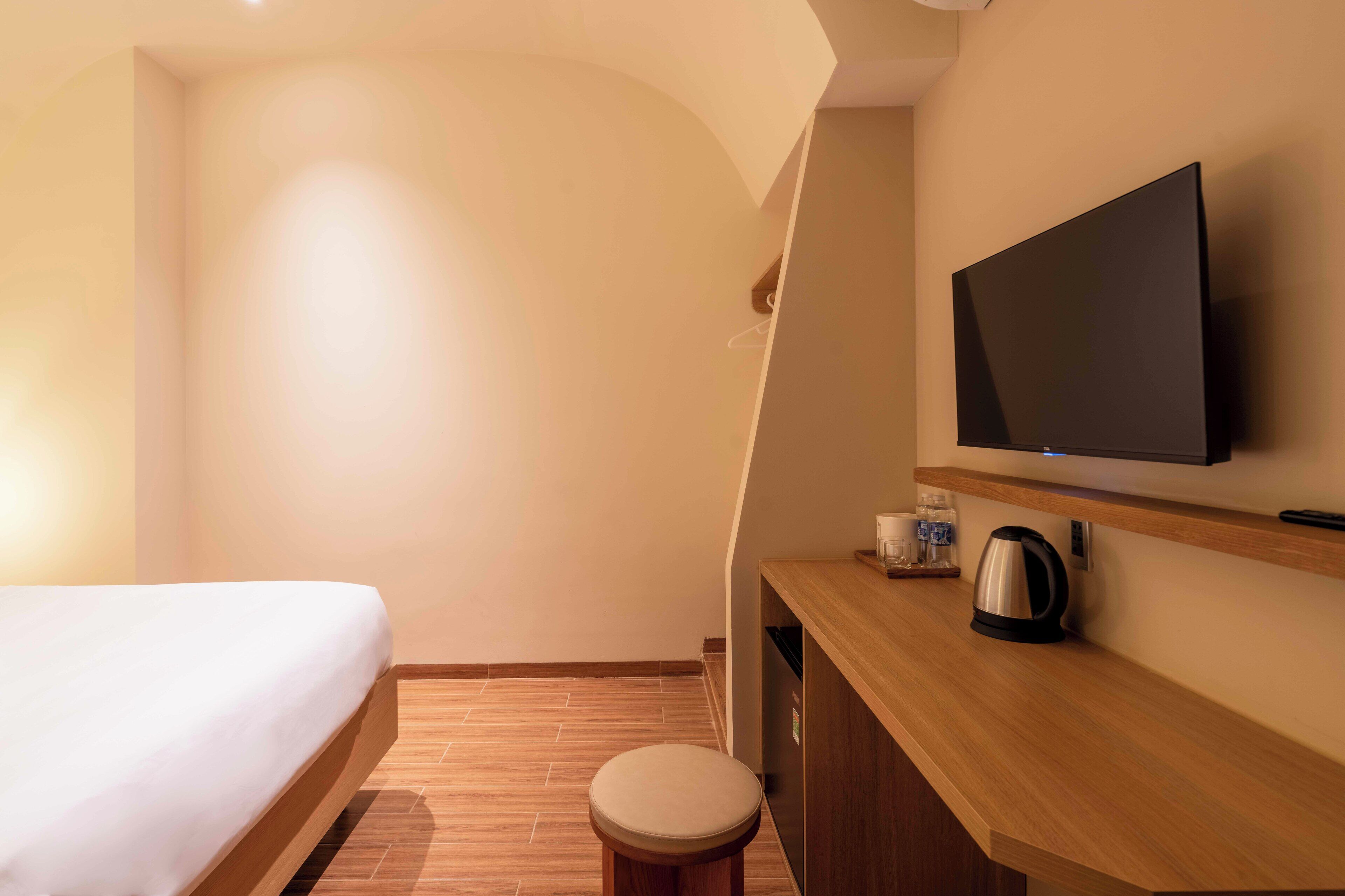 A hotel room with a bed, a wooden desk, a television, and a kettle.