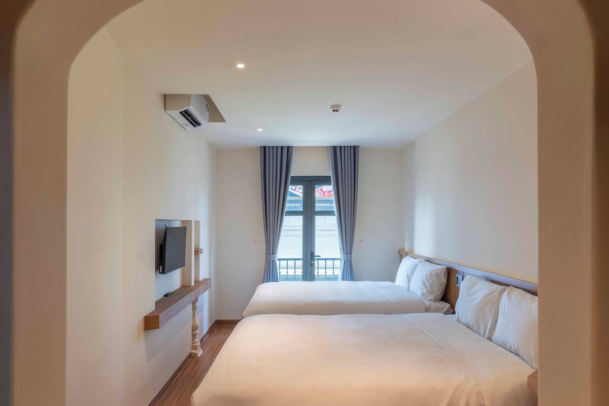 Une chambre d’hôtel avec un grand lit, un téléviseur posé sur une étagère en bois et une vue par la fenêtre, qui est dotée de rideaux.